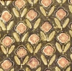 A close-up of a batik fabric pattern featuring repeating floral motifs in muted pink, olive green, and beige on a dark brown background.