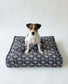 Dog sitting on a grey patterned dog bed against a white background
