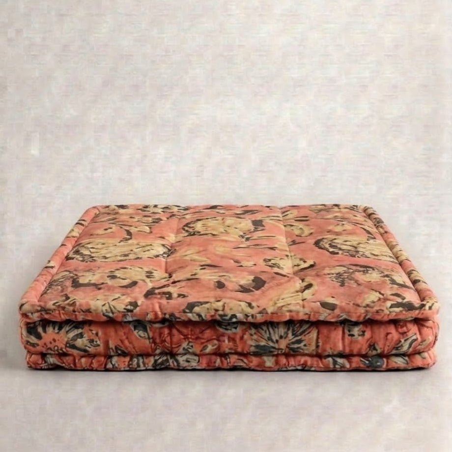 A square tufted floor cushion or mattress pad with a vintage floral pattern in dusty pink, beige, and dark brown, set against a neutral textured light gray background.