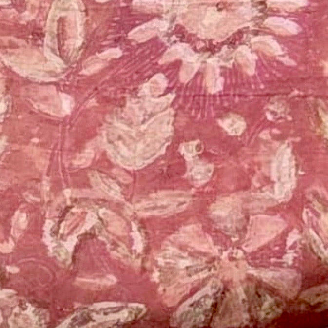 A close-up of a pink batik fabric with a distressed, vintage-style floral pattern in light pink and beige tones.