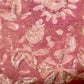 A close-up of a pink batik fabric with a distressed, vintage-style floral pattern in light pink and beige tones.
