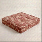 A tufted dog bed in a dusty rose and beige floral pattern, shown on a textured light gray background.