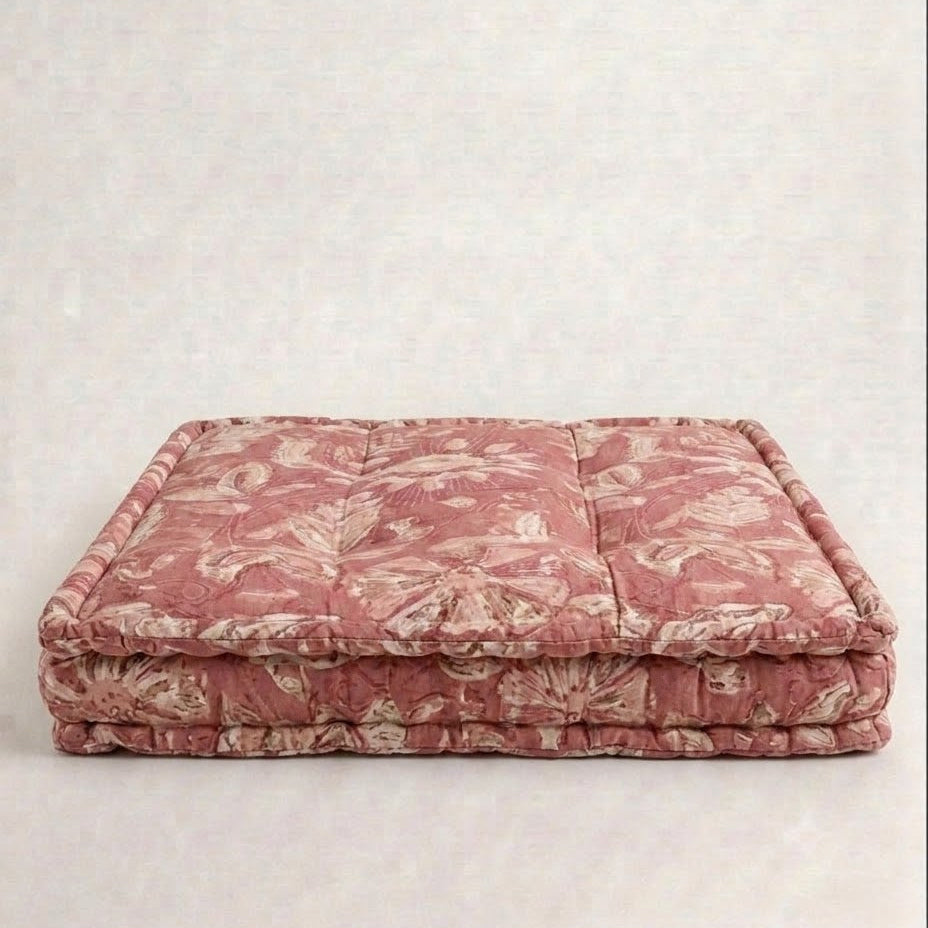 A pet bed with a dusty rose and beige floral toile pattern, set against a neutral textured light gray background.