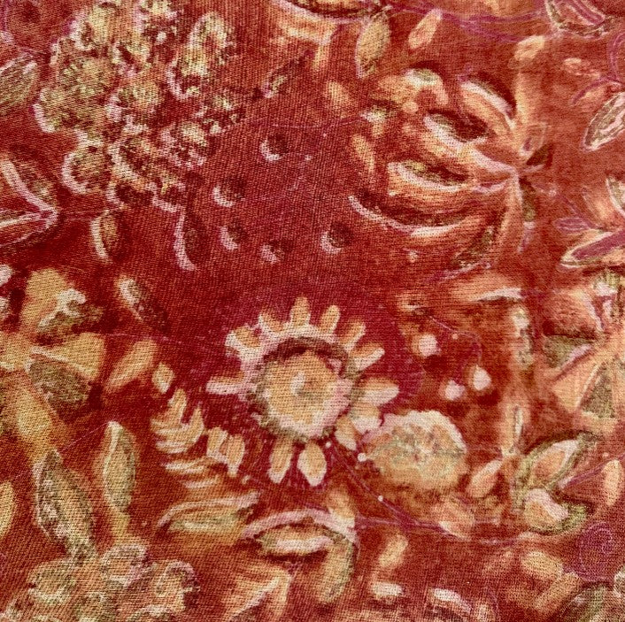 A close-up of a textured fabric with a distressed floral pattern in rust red, terracotta, and beige.